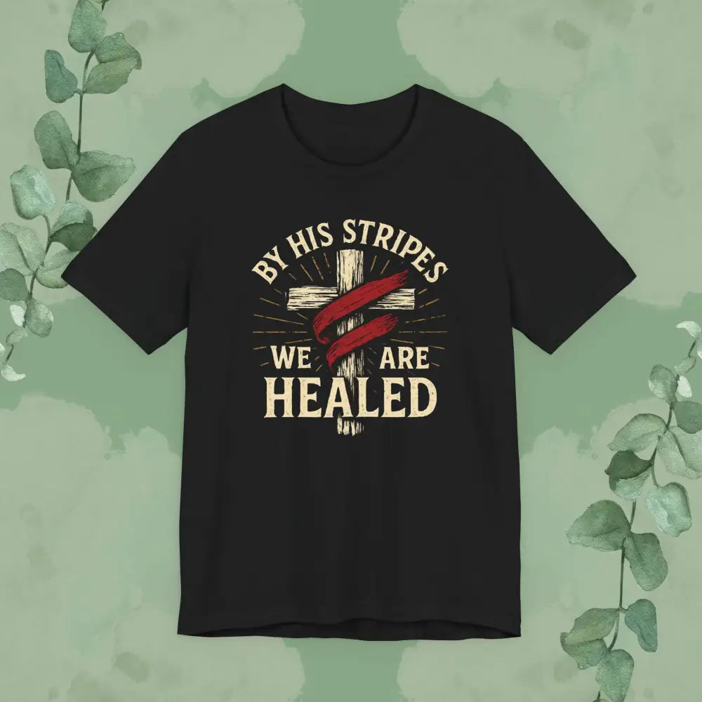 Black t-shirt with cross design and text 'By His Stripes We Are Healed' on a green background with leaves.