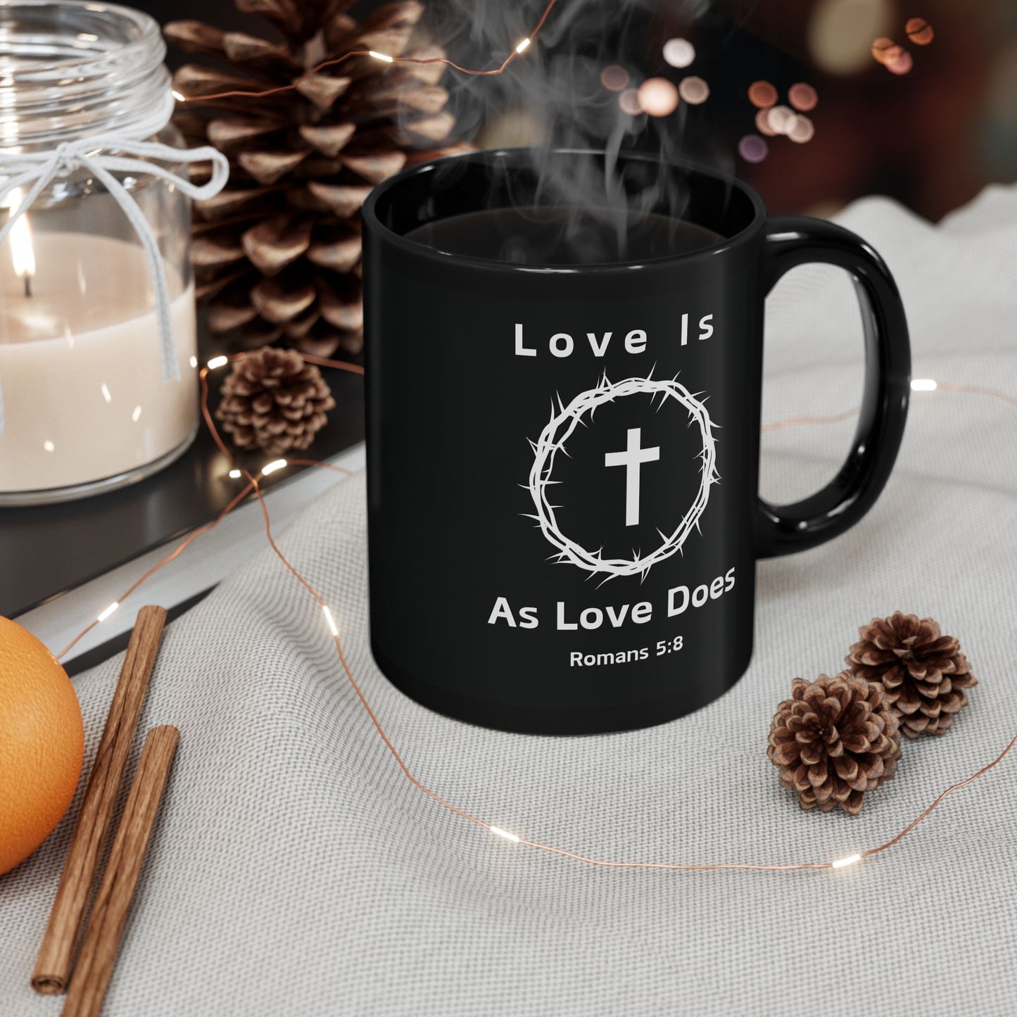 Black Christian mug with “Love Is As Love Does” Romans 5:8 cross design