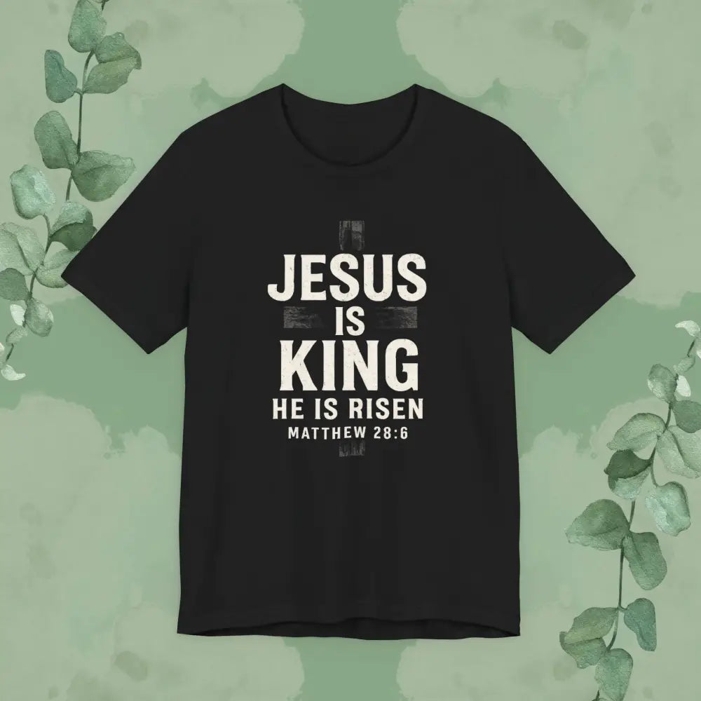 Black t-shirt with 'Jesus is King, He is Risen' text on a green background with leaves.