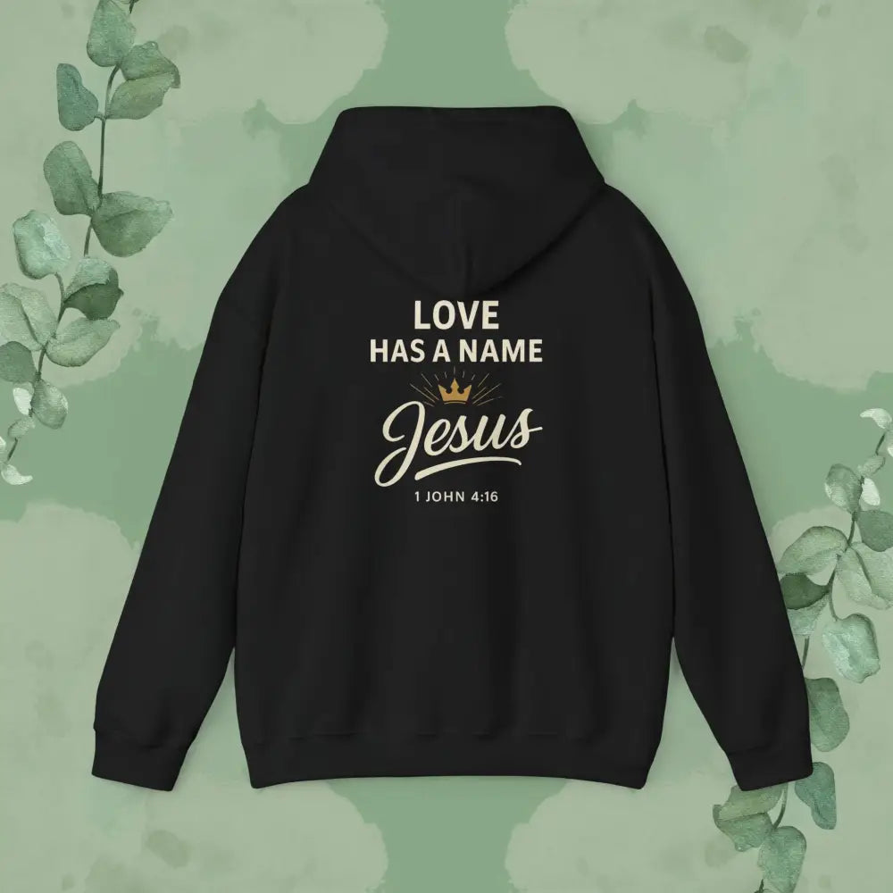 Black hoodie with 'Love Has a Name Jesus' text on the back against a green leafy background