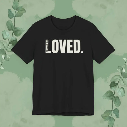 Black Christian T-shirt with bold white text that reads “LOVED” and a vertical Romans 5:8 Bible verse design by True Vine Design.
